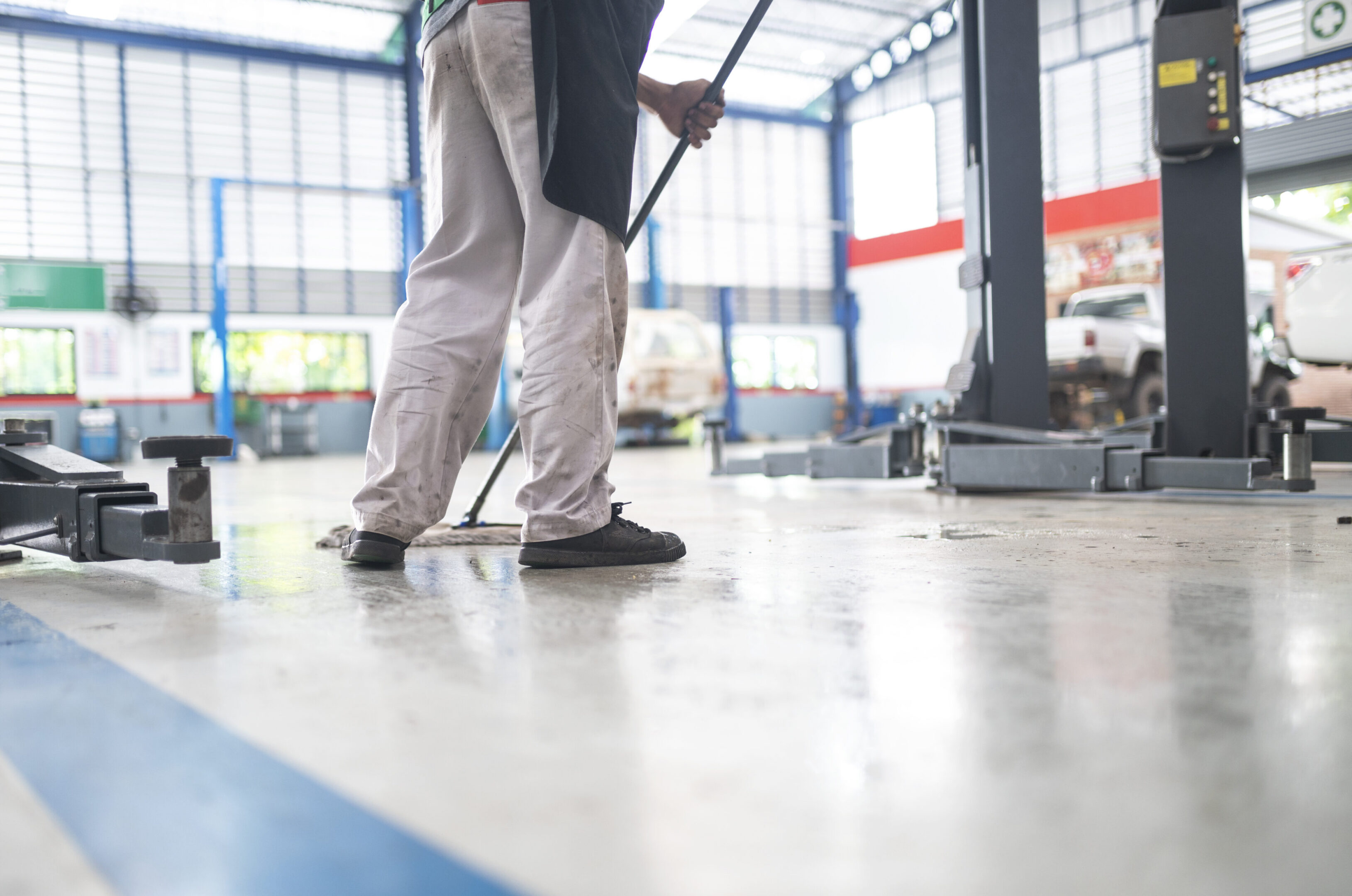 mechanic in auto repair center Cleaning using a mop Squeeze water from the epoxy floor. in the car repair service center