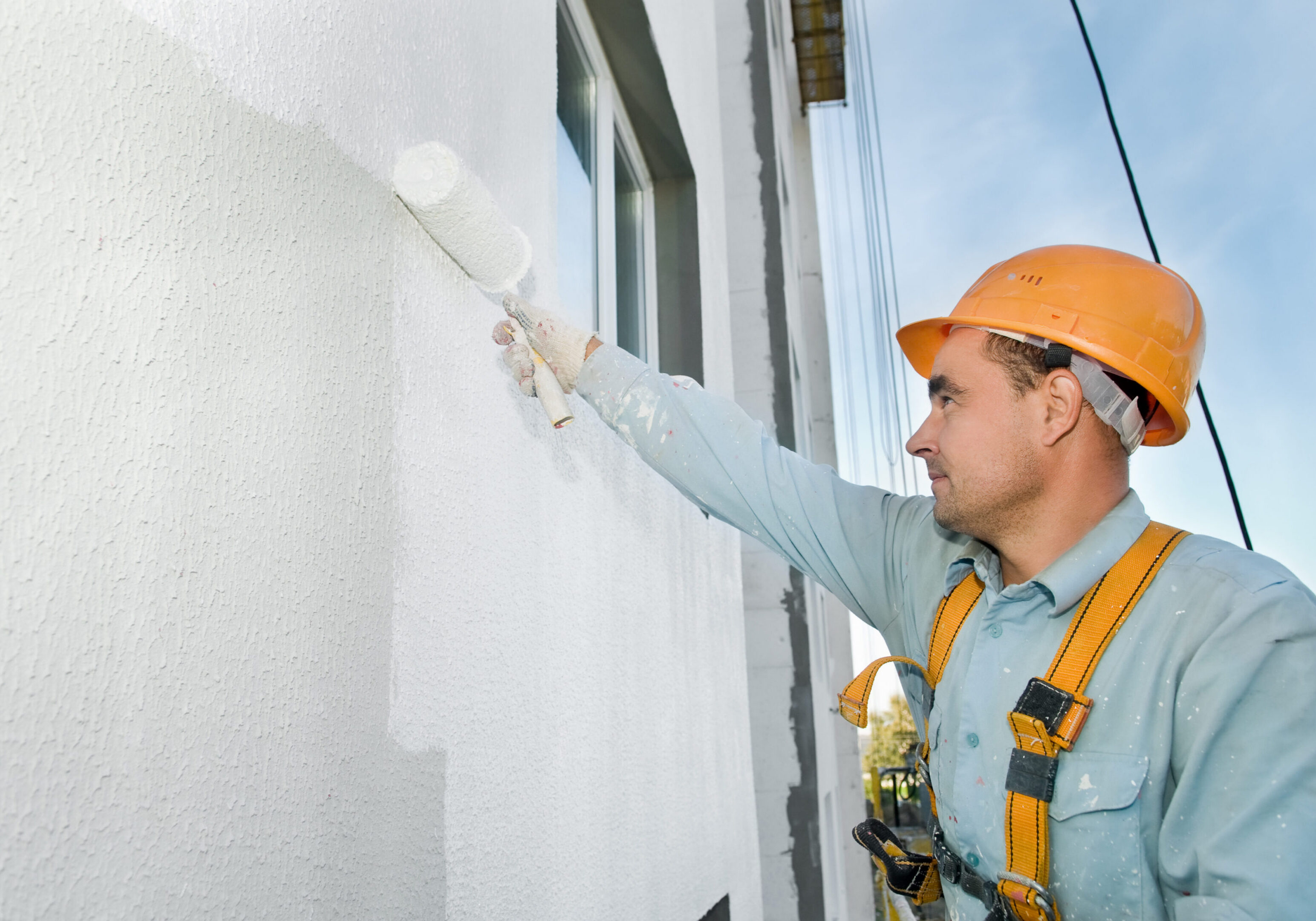 builder worker painting facade of building house with roller